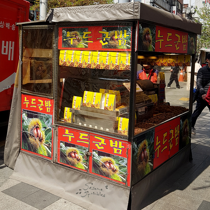 Small food stall with advertisement for "nudeu gun bam" (누드군밤), peeled and roasted chestnuts.