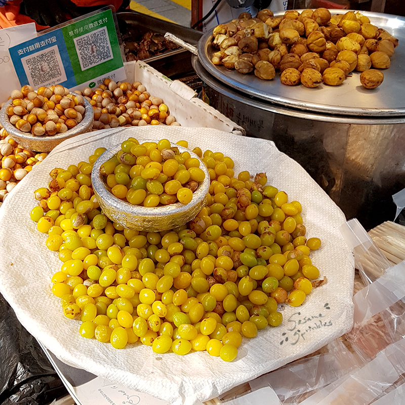 Yellow roasted ginkgo seeds, raw ginkgo seeds and chestnuts on display at a food stall.